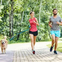 Para biegaczy i ich piesek cieszą się wspólnymi psimi sportami na ścieżce w parku.